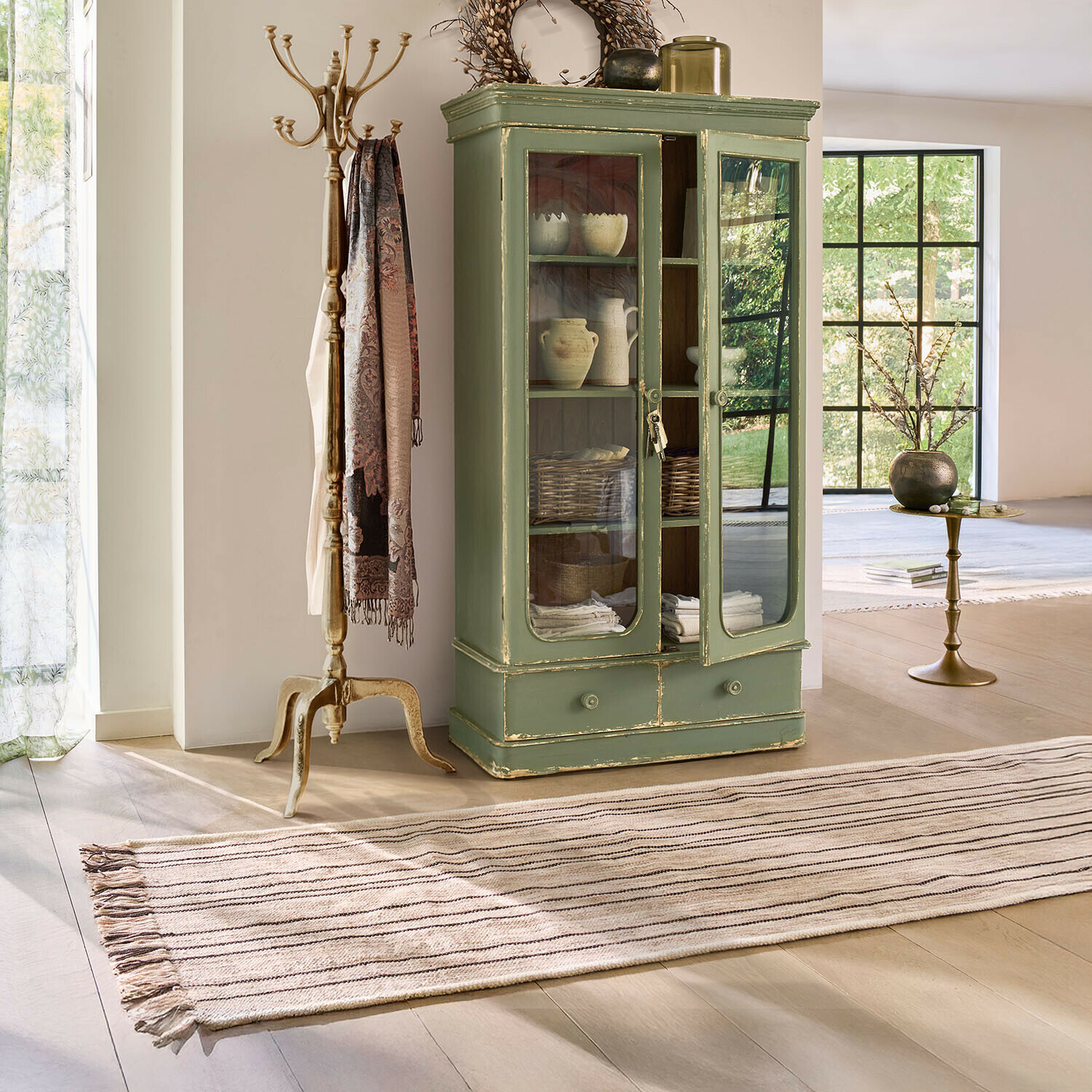 Groene houten vitrinekast met glazen deuren en lade in lichte vintage woonkamer