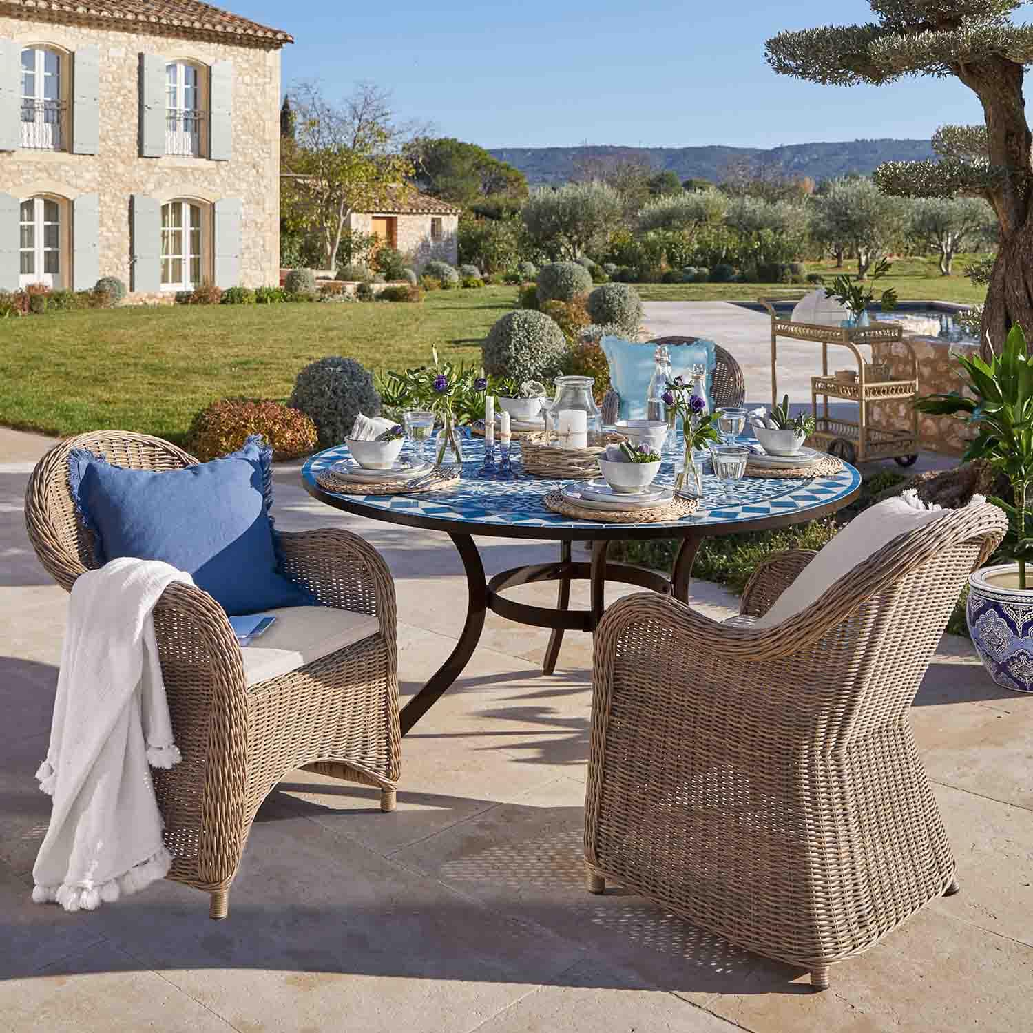 Ronde mozaïektafel in blauw met beige rotan stoelen op zonnig tuinterras