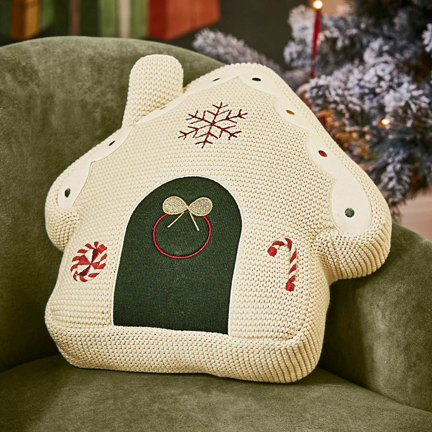 Decoratief kussen in huisvorm van crème gebreide stof met kerstmotieven en groene details op groene stoel