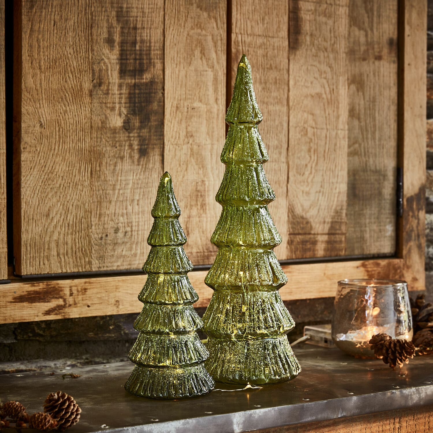 Ledkerstboom set van 2 Merrton Twee groene glazen kerstboomdecoraties met LED-verlichting tegen houten achtergrond, feestelijke versiering