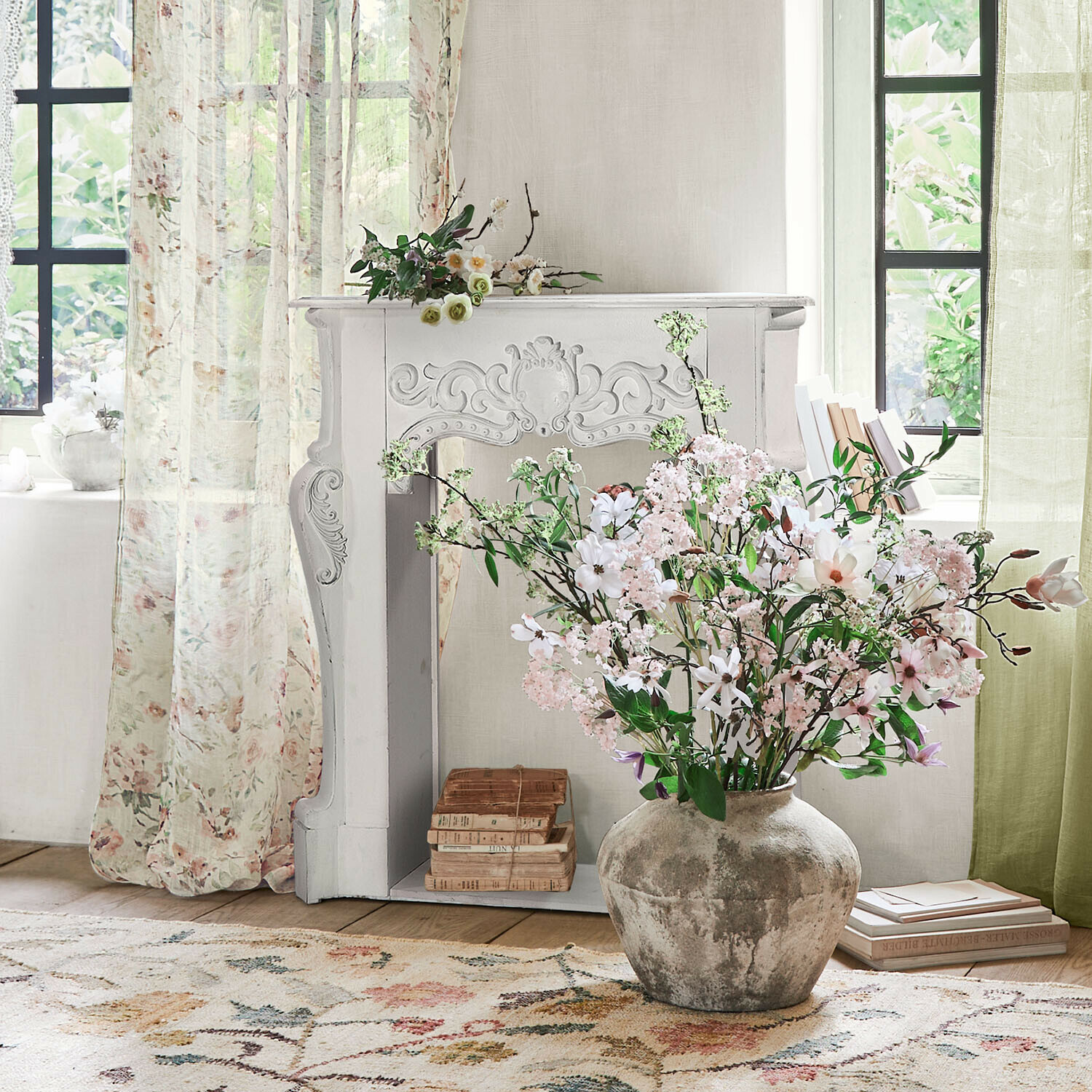 Grote grijze keramische vaas met boeket roze en witte bloemen in lichte kamer met decoratieve schoorsteen