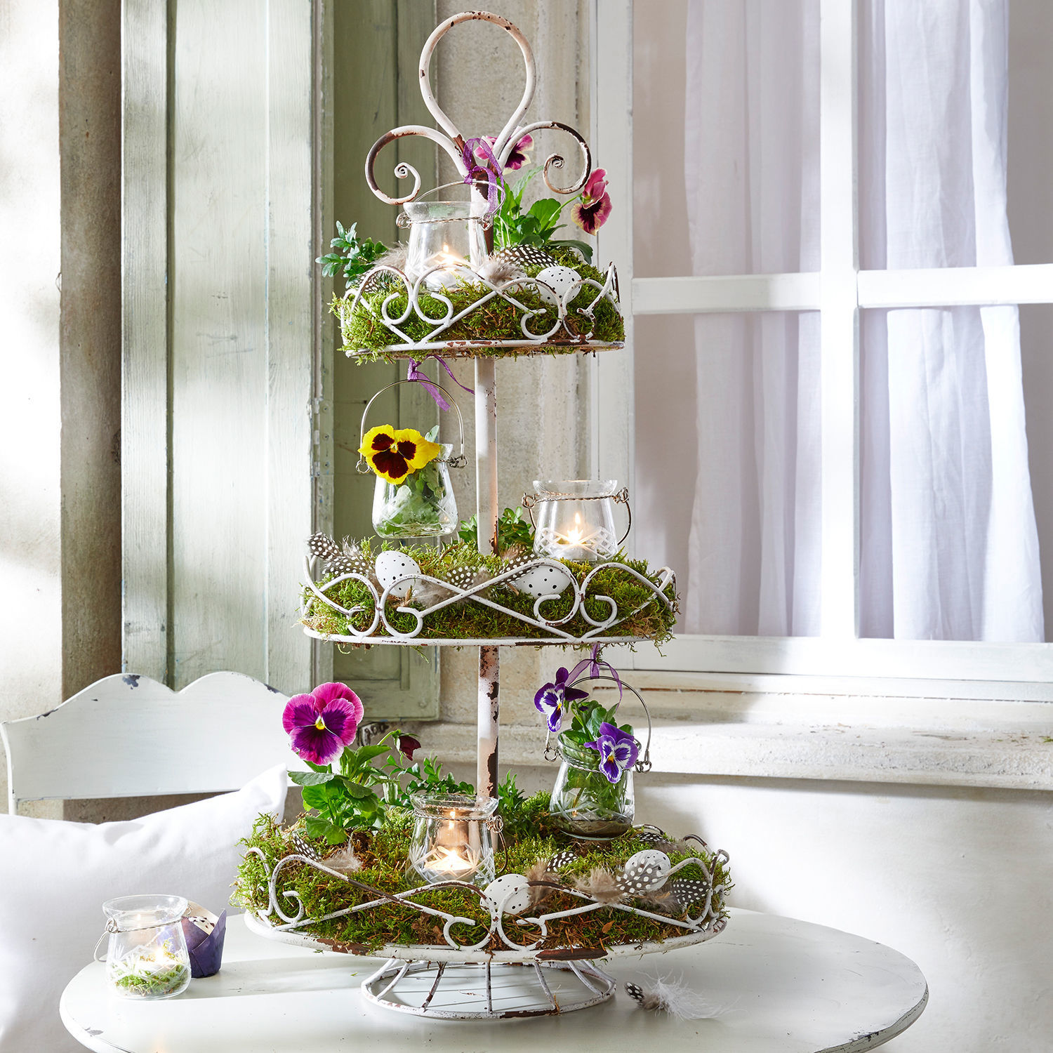 Etagère Julye Drie verdiepingen wit metalen etagère met mos, bloemen en kaarsen als decoratie op witte tafel