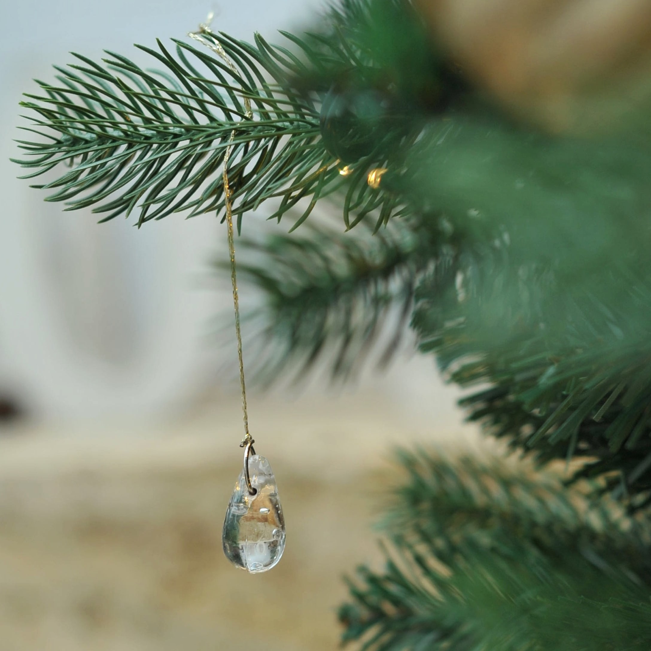 Transparante glazen hanger aan gouden draad aan groene kerstboomtak