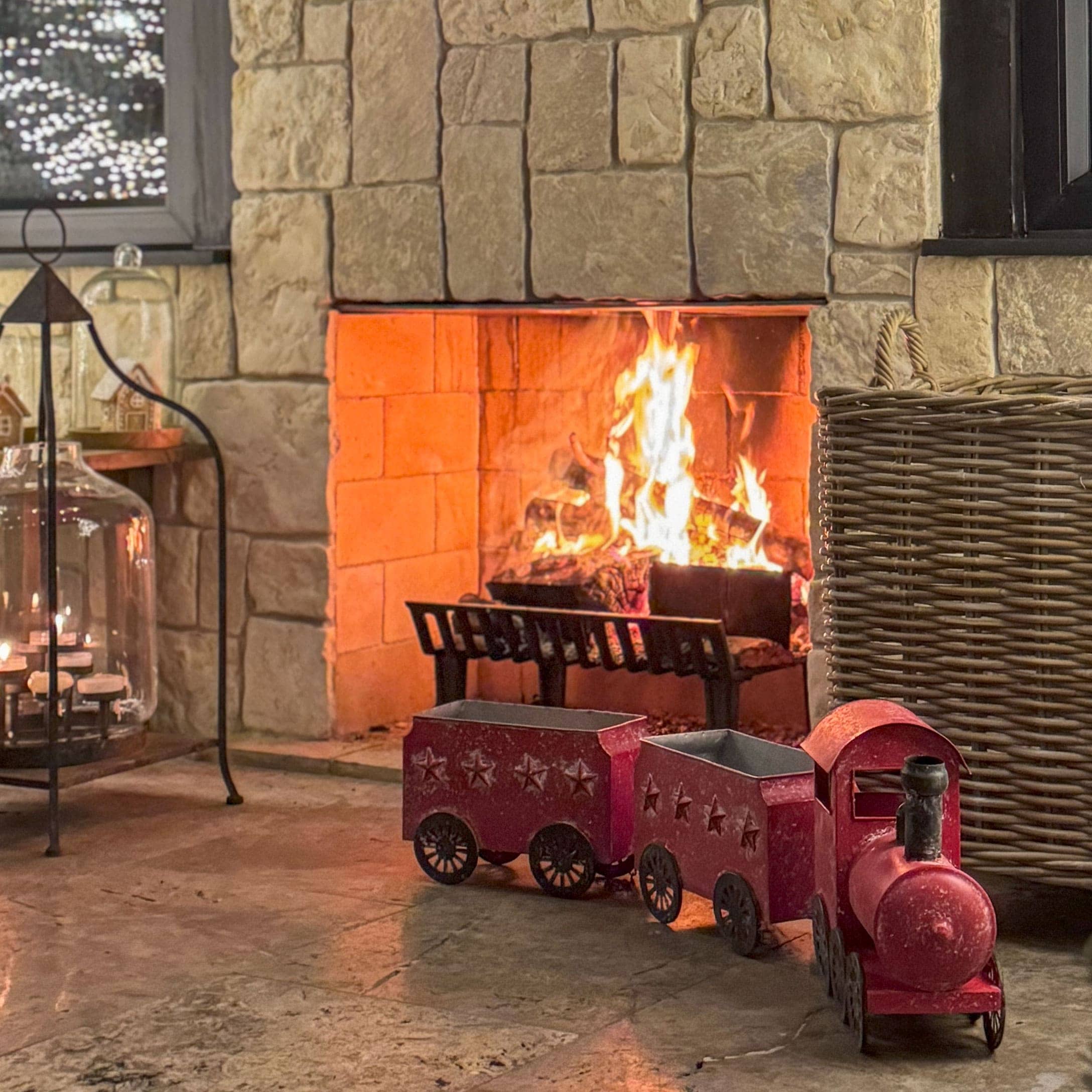 Rode metalen decoratieve trein bij stenen open haard met brandend hout, feestelijke sfeer