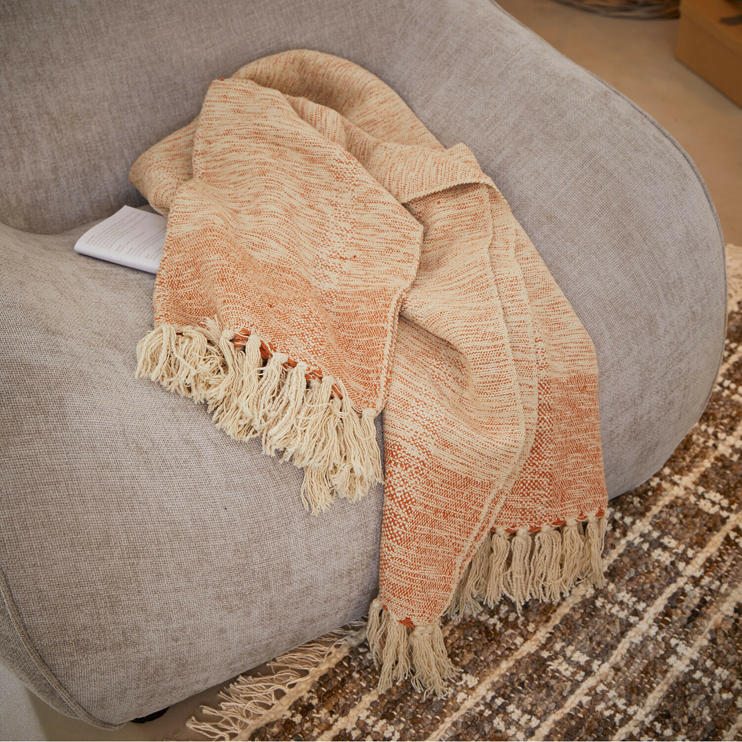 Plaid Winlow Beige-oranje deken met franjes op een grijze stoel, zacht materiaal voor interieurdecoratie