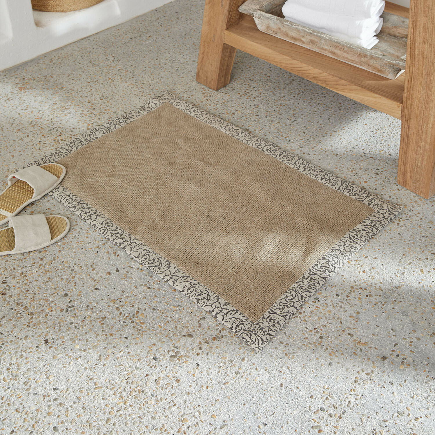 Badmat Falmont Beige mat van natuurlijk materiaal met decoratieve grijze rand op lichte stenen vloer