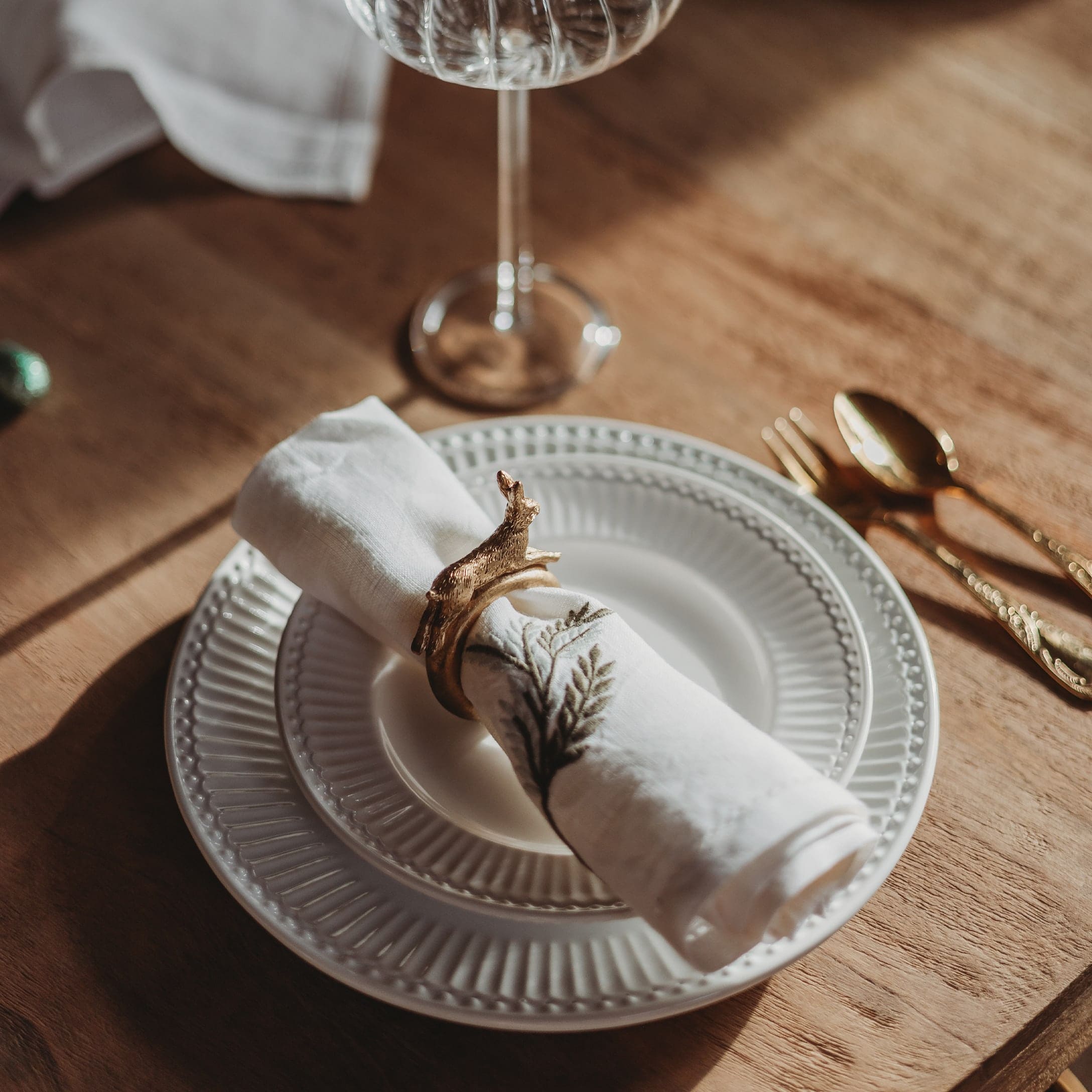 Witte keramische bord met versierde servet en gouden servetring op houten tafel