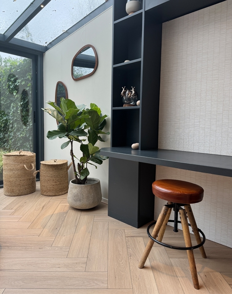 Modern interieur met zwart bureau, bruine leren kruk en betonnen pot met groene plant