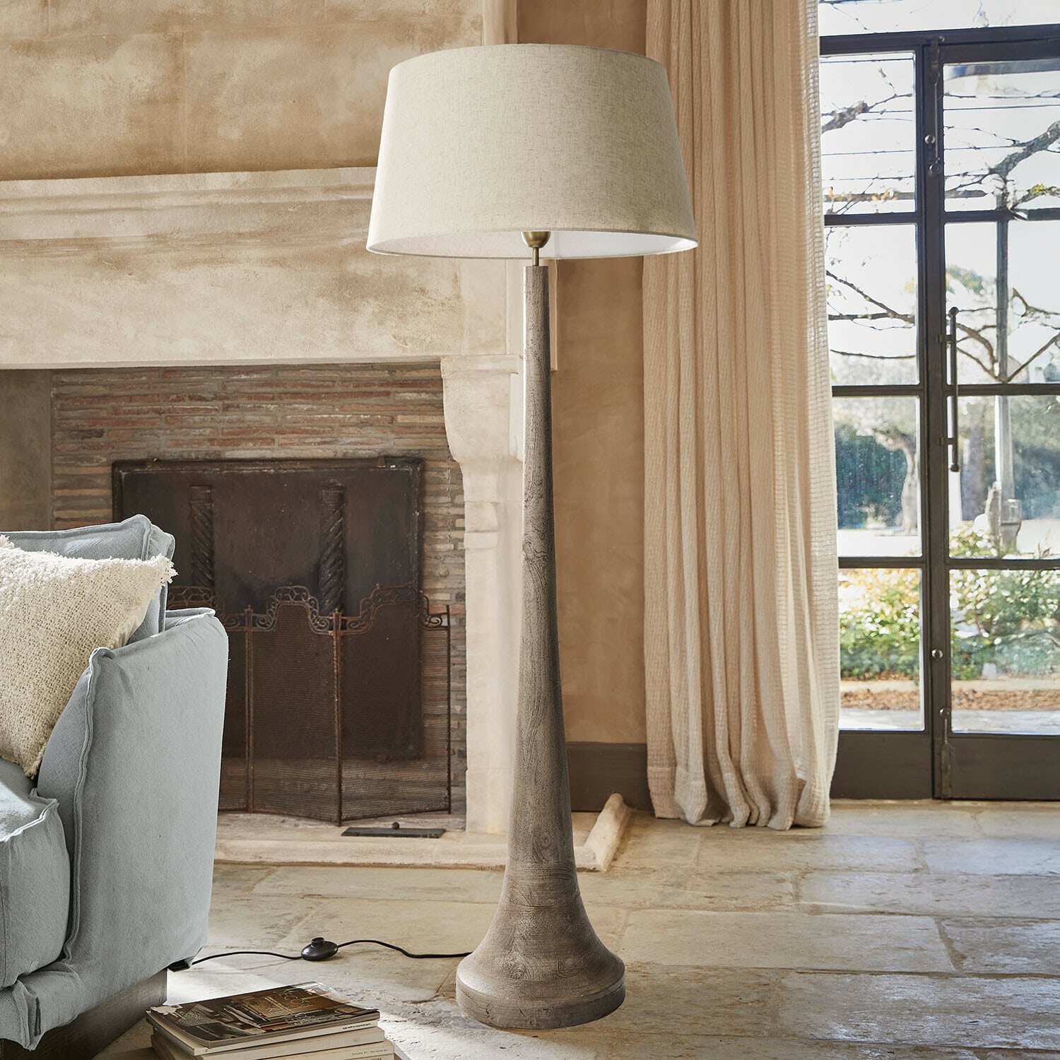 Staande lamp met houten voet en beige kap in een gezellige woonkamer met open haard en bank