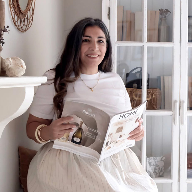 Vrouw in wit shirt en lichte rok leest woonmagazine in lichte kamer met houten kast