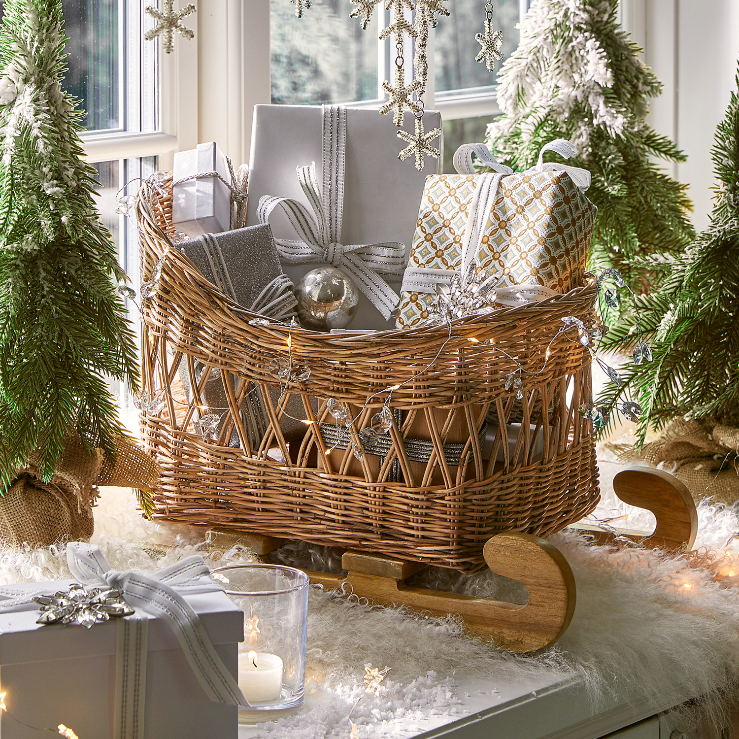 Rieten slee met houten runners gevuld met zilveren en witte kerstcadeaus als decoratie