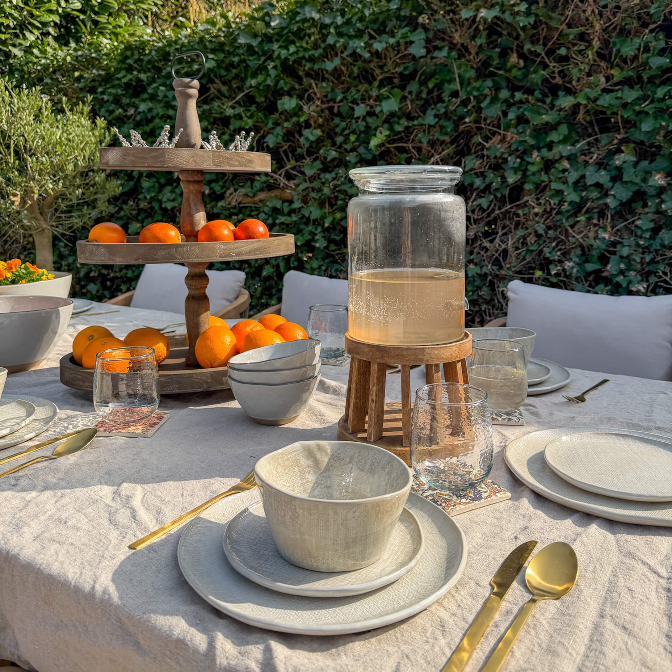 Tuin tafel met crèmekleurig keramiek, gouden bestek en houten fruitstandaard