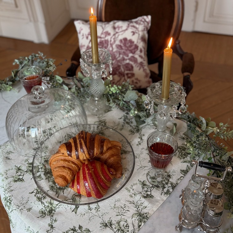 Glazen bord met croissant en gebak op tafel met wit tafelkleed, twee gouden kaarsen in kristallen kandelaars