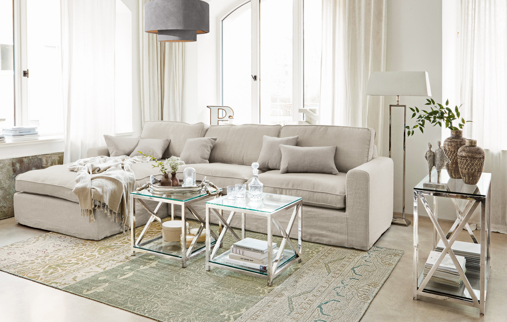 Beige klassieke linnen bank met kussens en glazen tafels op metalen frame in lichte woonkamer