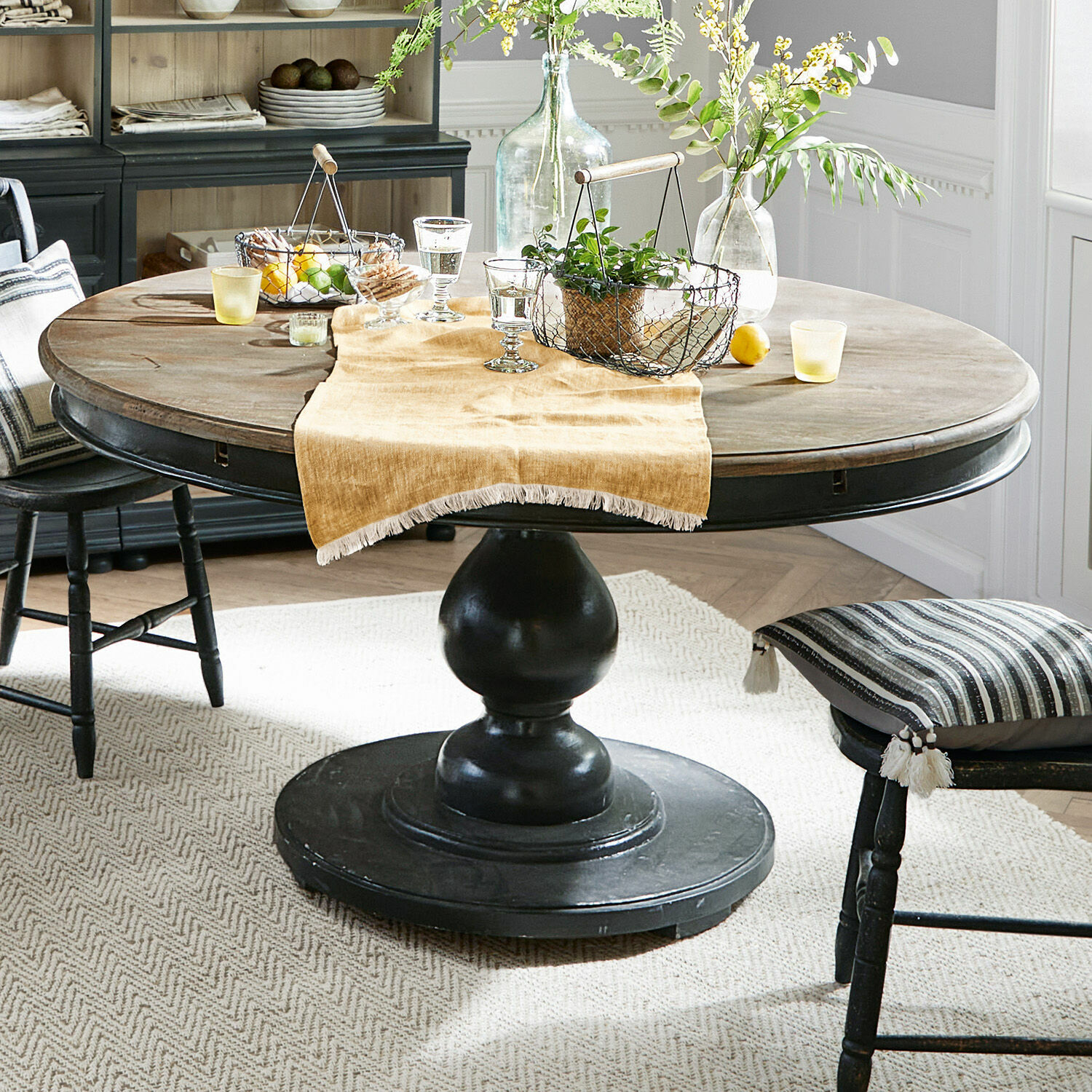 Tafel Shrewsbury Ronde houten tafel met zwarte voet en decoratie op beige loper in eetkamer