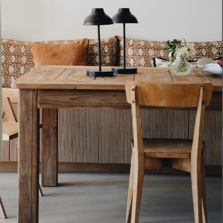 Houten tafel met twee zwarte lampen en bloemen in vaas voor bank met oranje kussens
