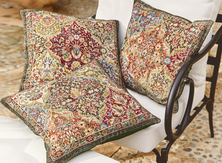 Drie decoratieve kussens met oosters patroon in warme kleuren op een witte metalen stoel