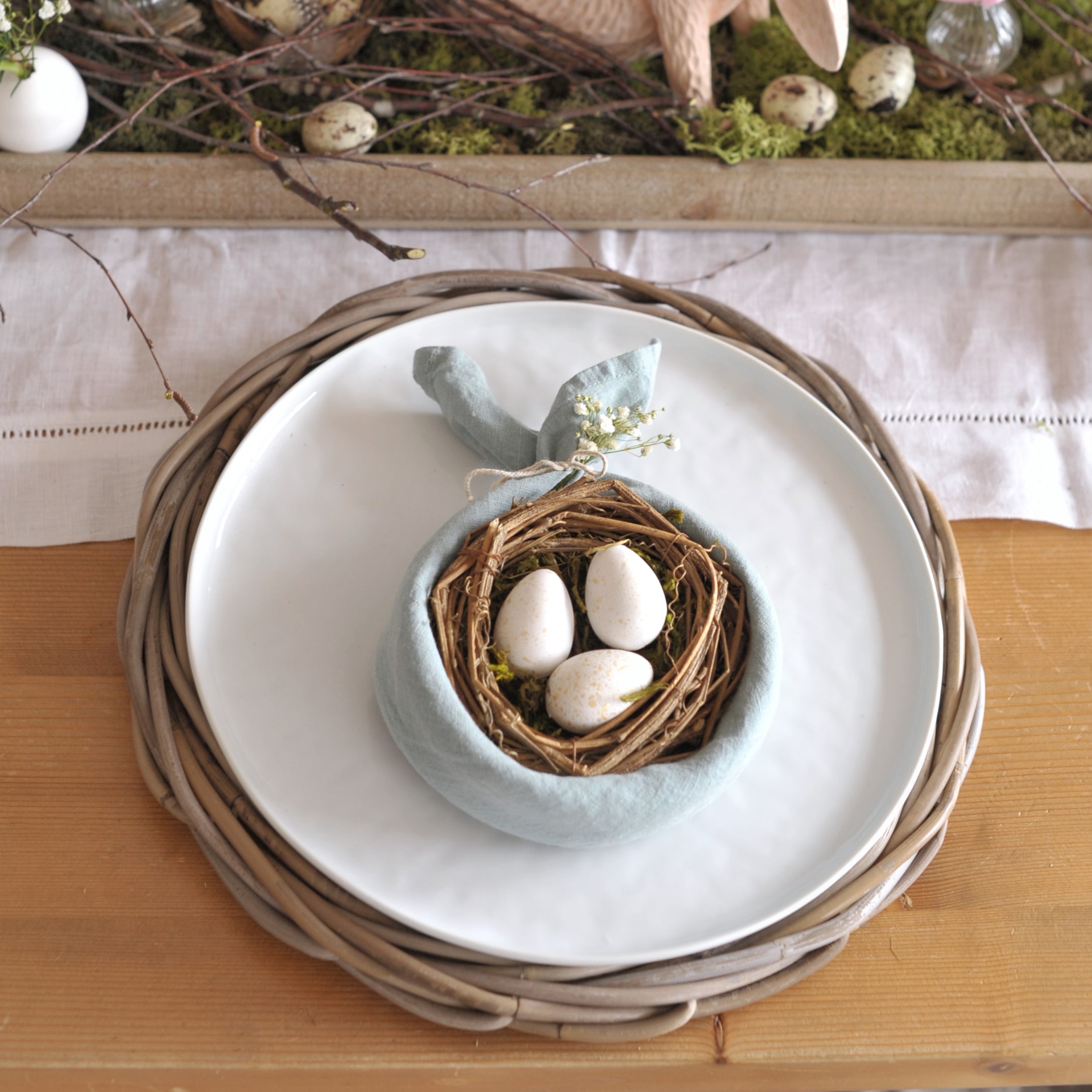 Tafelversiering met wit bord, gevlochten onderzetter en servet met nest en eieren
