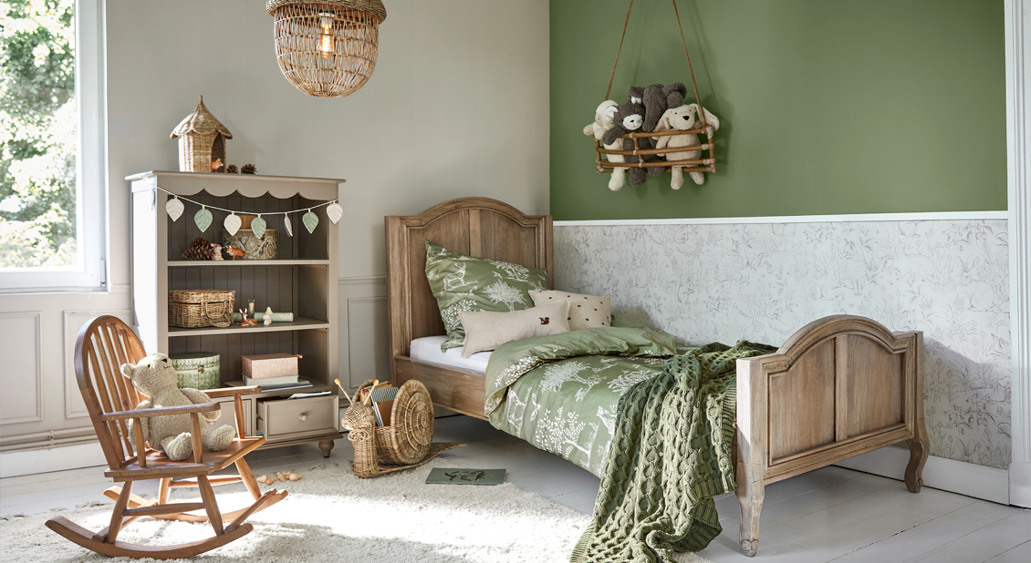 Houten kinderbed met groene beddengoed en knuffels in een gezellige kinderkamer met natuurlijke decoratie