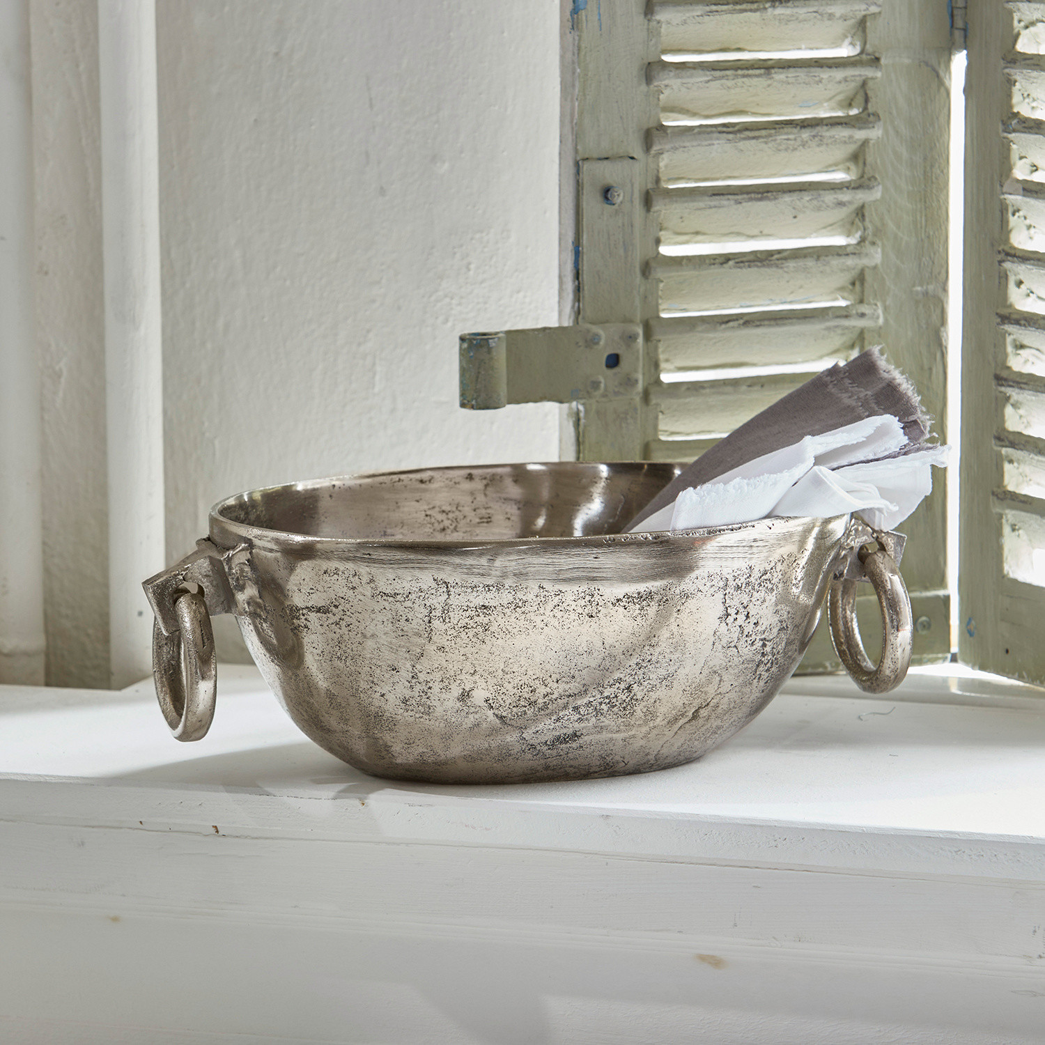Decoratieve metalen schaal in zilverkleur met handvatten en linnen doeken op vensterbank