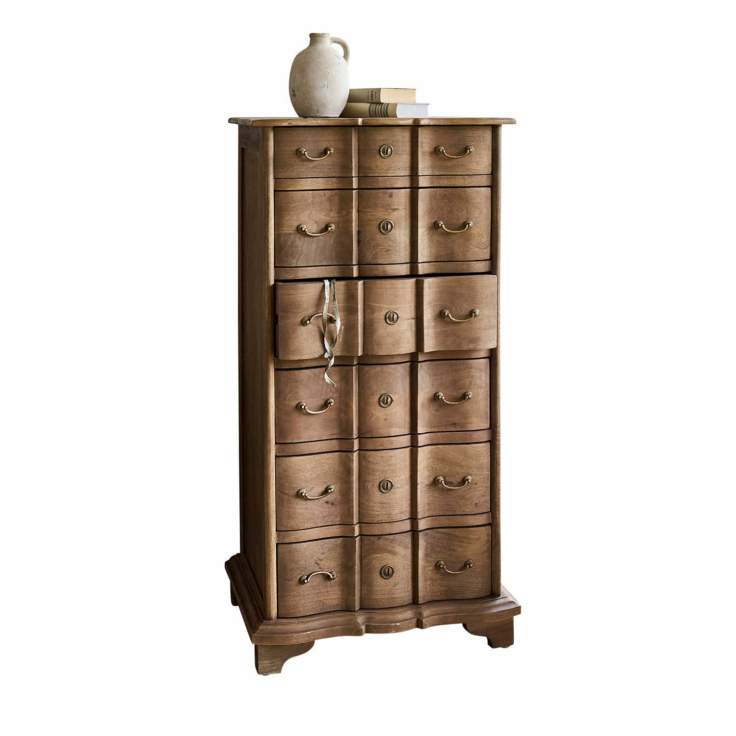 Hoge kast van natuurlijk hout met meerdere lades en keramische kruik op boeken