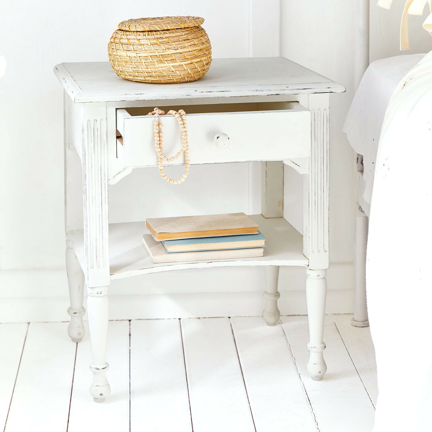 Witte houten nachtkastje met lade en plank, rustieke stijl met rieten mand en boeken