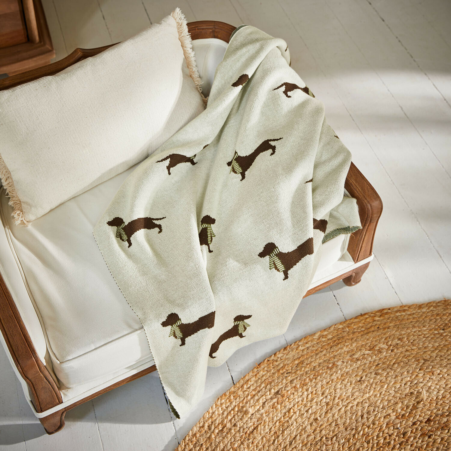 Huisdierendeken Brisette Beige deken met teckelpatroon op witte houten bank met kussen met franjes