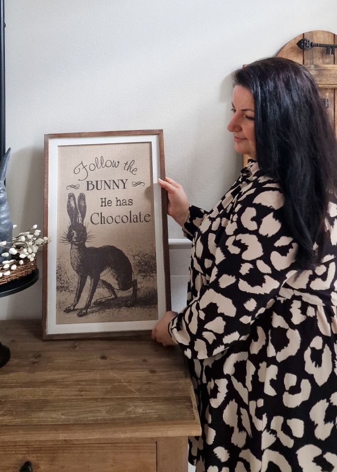 Vrouw houdt lijst vast met afbeelding van konijn en tekst over chocolade op houten tafel
