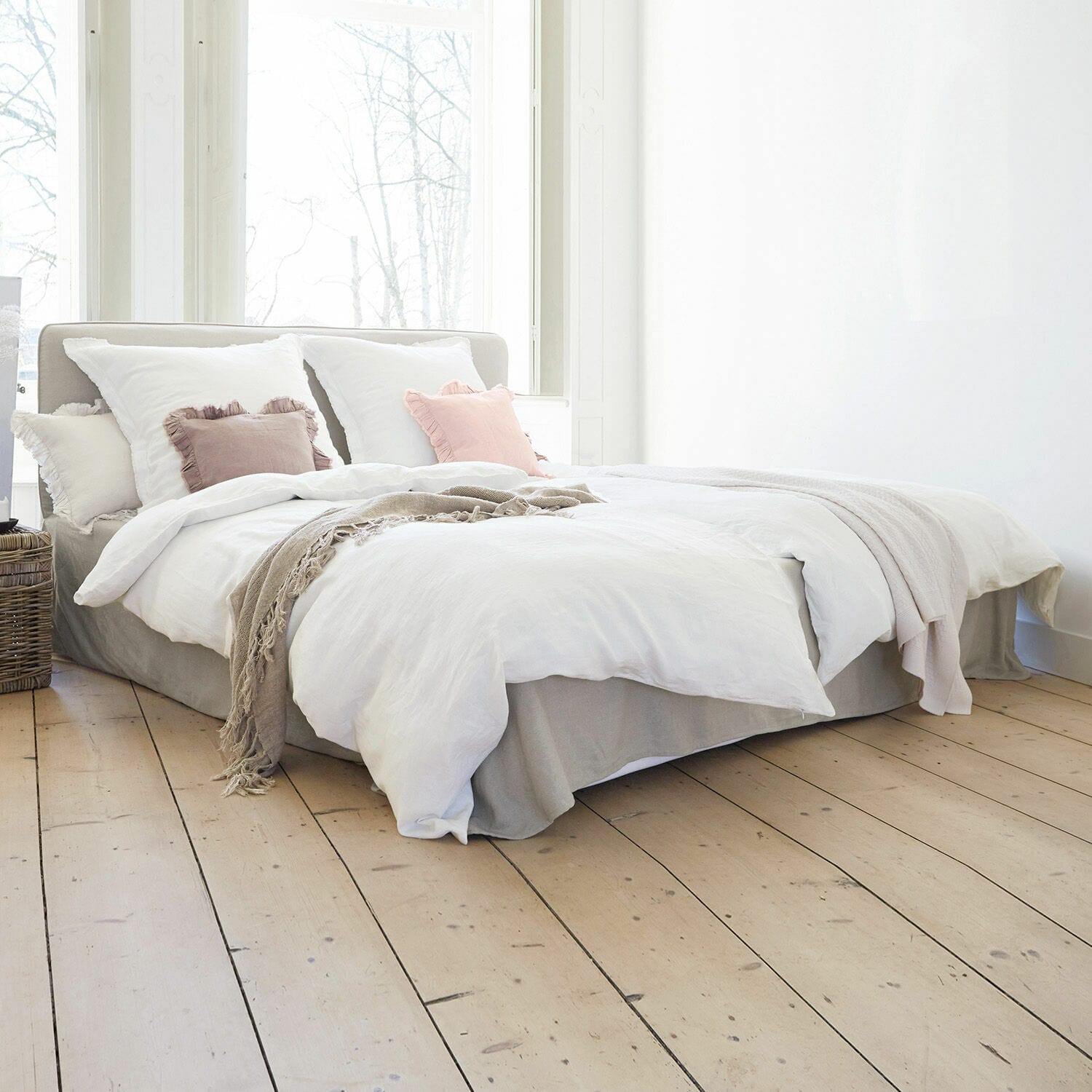 Bed Aubrianne Lichtgrijs gestoffeerd bed met wit beddengoed en pastelkleurige kussens in lichte slaapkamer