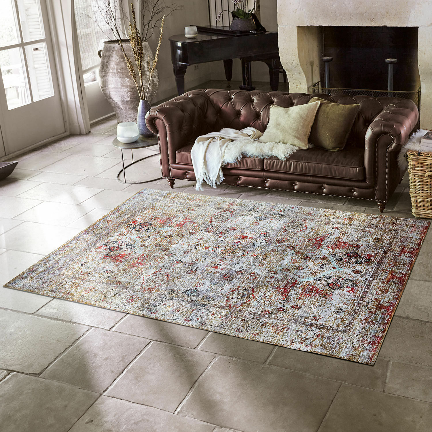 Decoratief vloerkleed in lichte kleuren met vintage patroon op stenen vloer in woonkamer met bruine leren bank