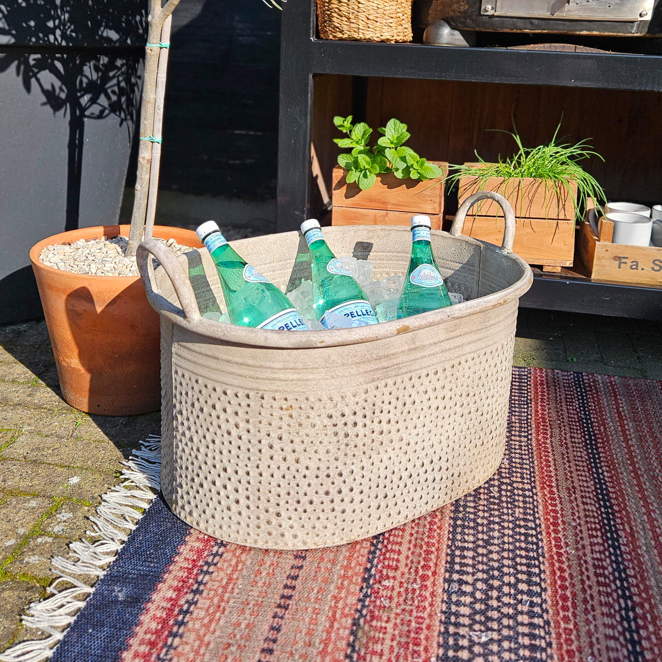 Beige stoffen mand met handvatten gevuld met mineraalwaterflessen op ijs buiten op tapijt