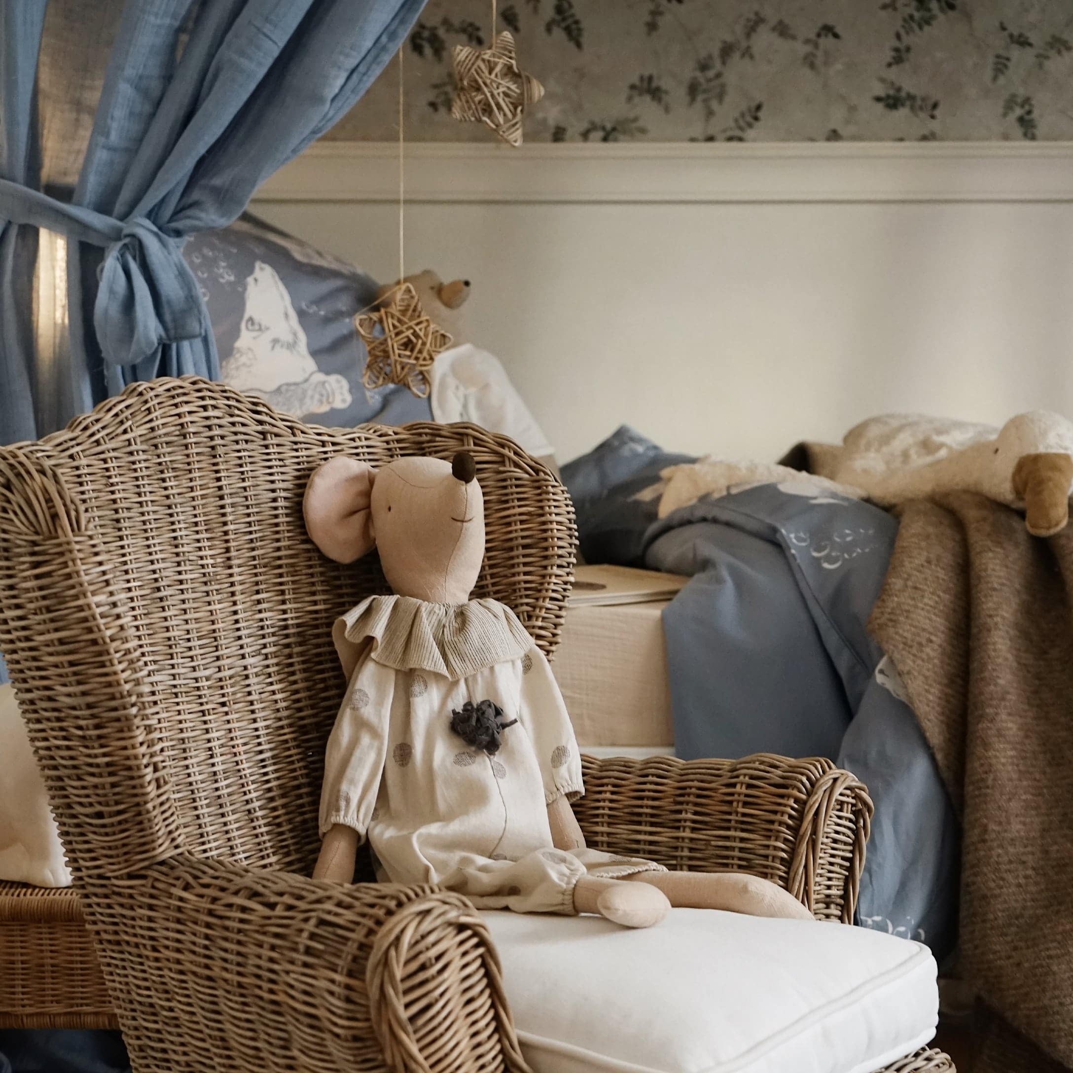 Natuurlijke rotan stoel met licht kussen en beige pluchen muis in kinderkamer