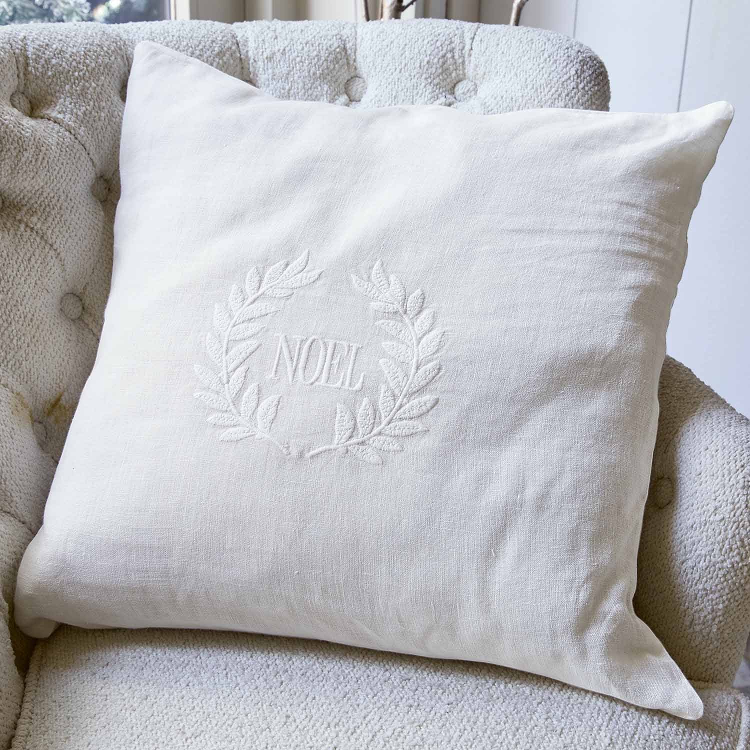 Witte linnen kussen met NOEL borduurwerk en decoratieve krans op lichte stoel, kerstaccessoire