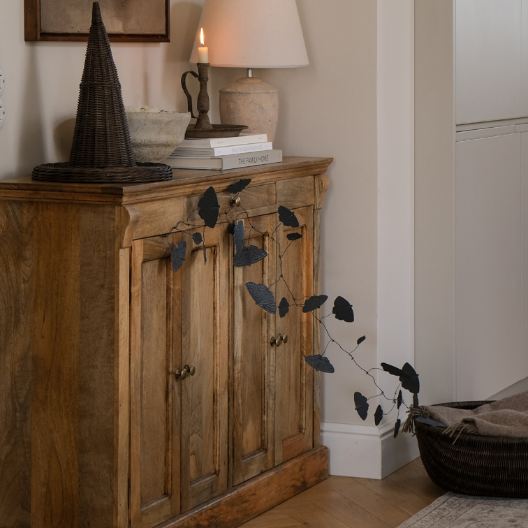 Houten dressoir met zwarte bladeren slinger en tafellamp in een gezellige kamer
