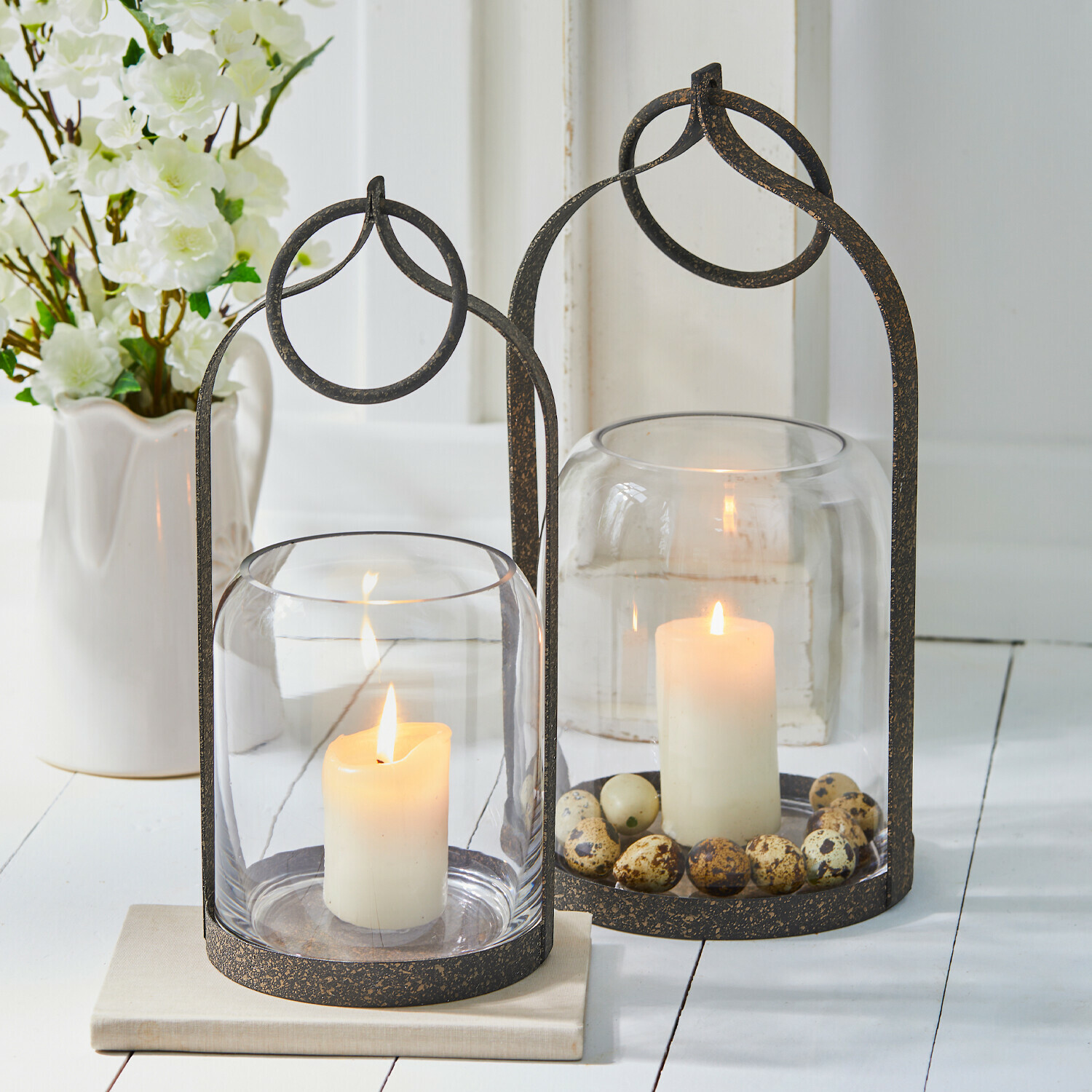 Twee metalen lantaarns met helder glas en witte kaarsen, versierd met natuurlijke eieren