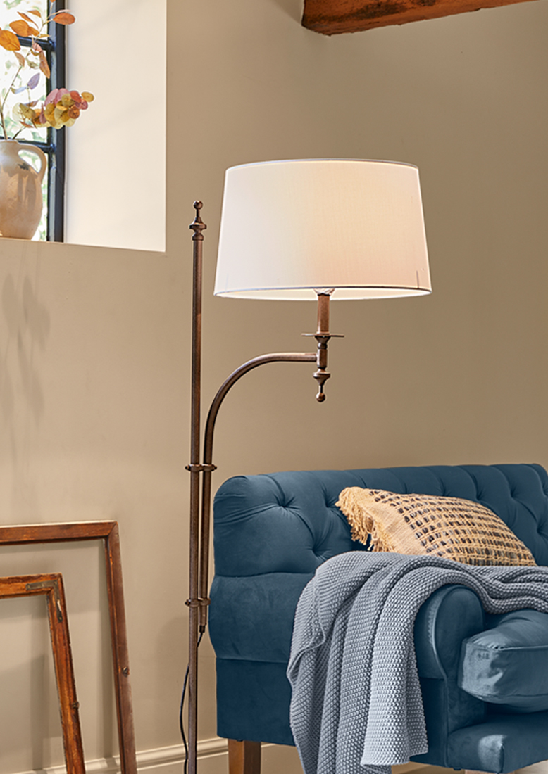 Staande lamp met metalen frame en witte kap naast een blauwe bank met gebreide deken