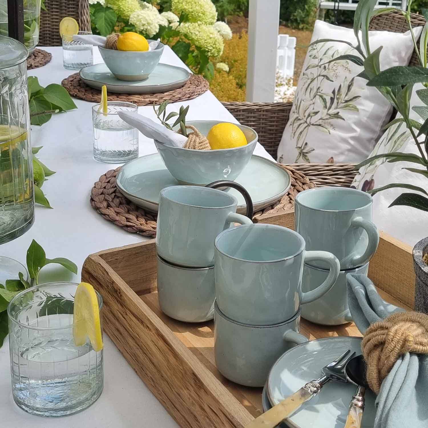 Set lichtblauw keramisch servies op houten dienblad met citroenen en glazen water