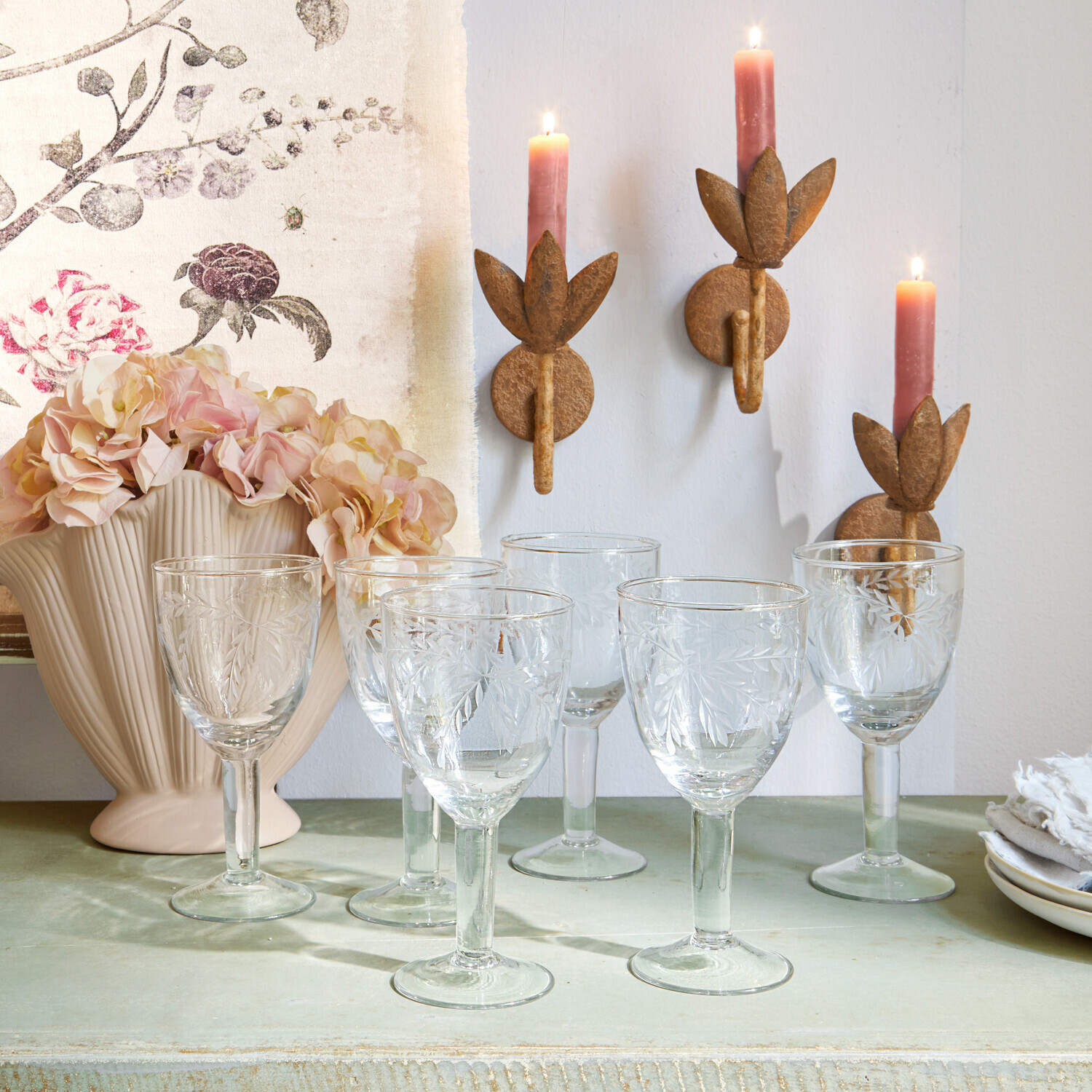 Set van zes glazen met gegraveerd bladmotief op groene tafel met kaarsen en bloemen als decoratie