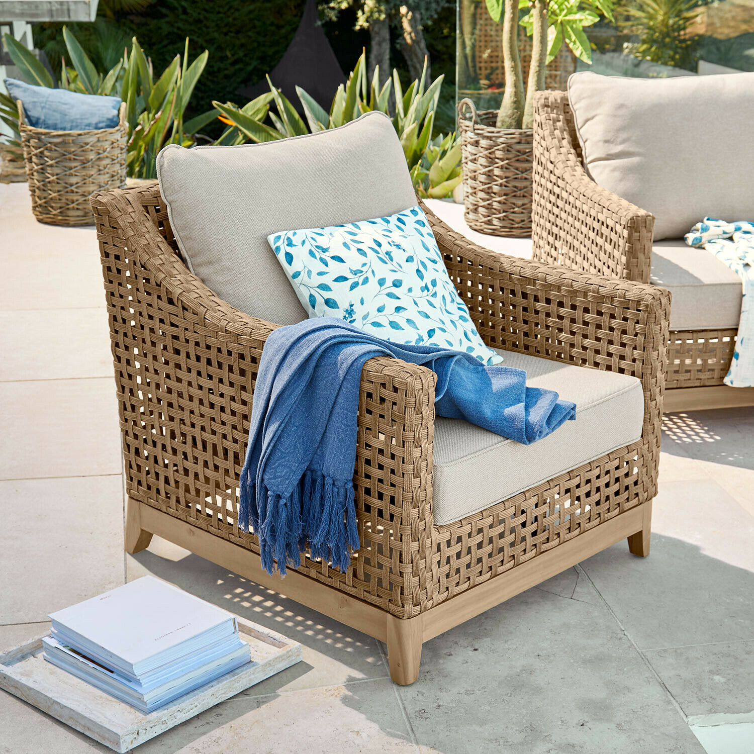 Tuinfauteuil van natuurlijk vlechtwerk met lichtgrijze kussens en blauwe deken