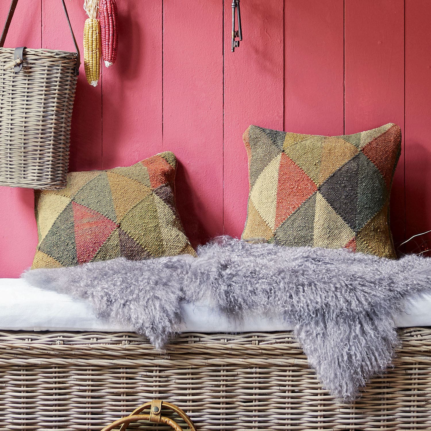 Twee kleurrijke kussens met geometrisch patroon op een rieten bank met grijze bontdeken