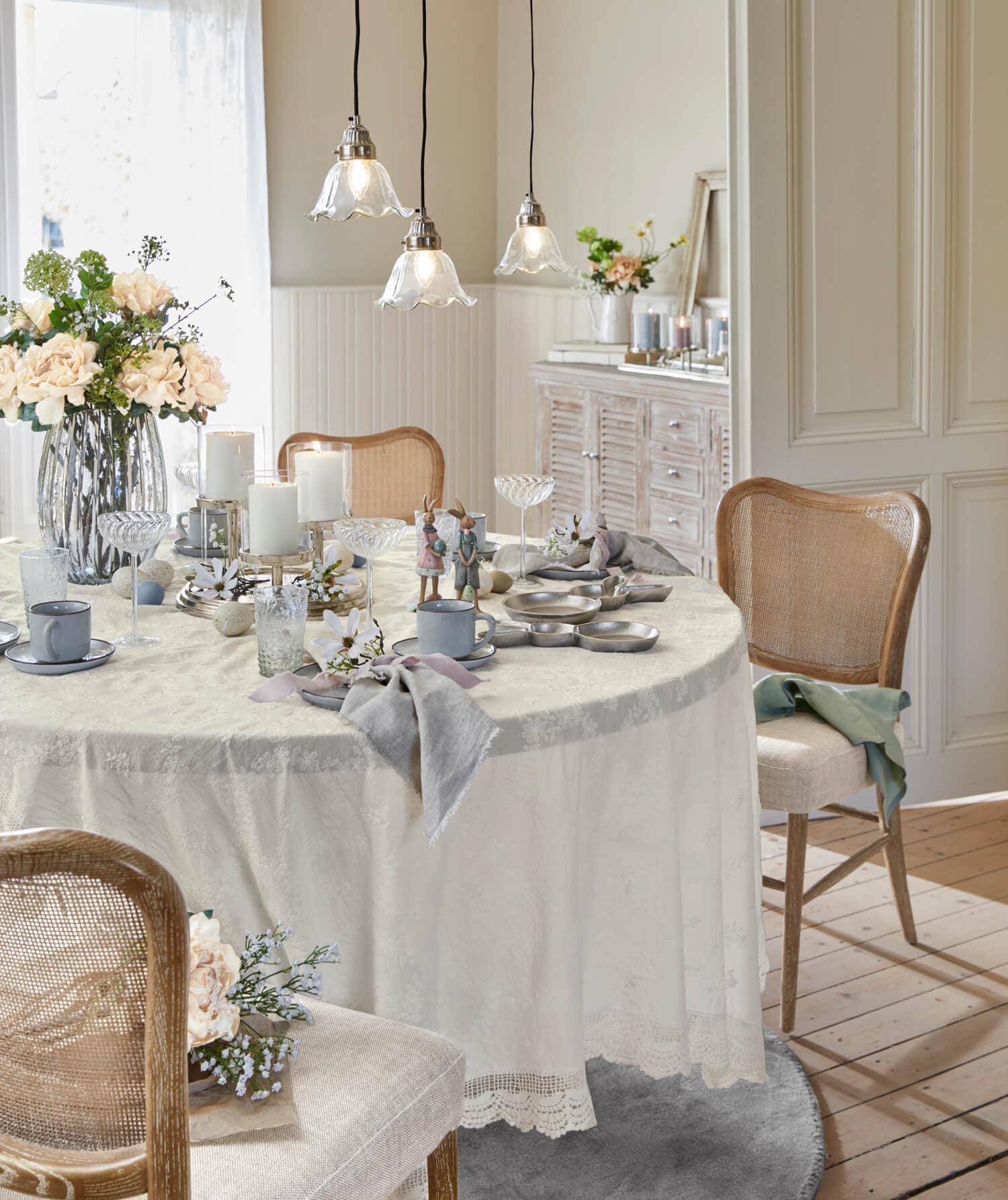 Lichte tafel met crèmekleurig tafelkleed en rustieke decoratie, houten stoelen en bloemen in lichte eetkamer