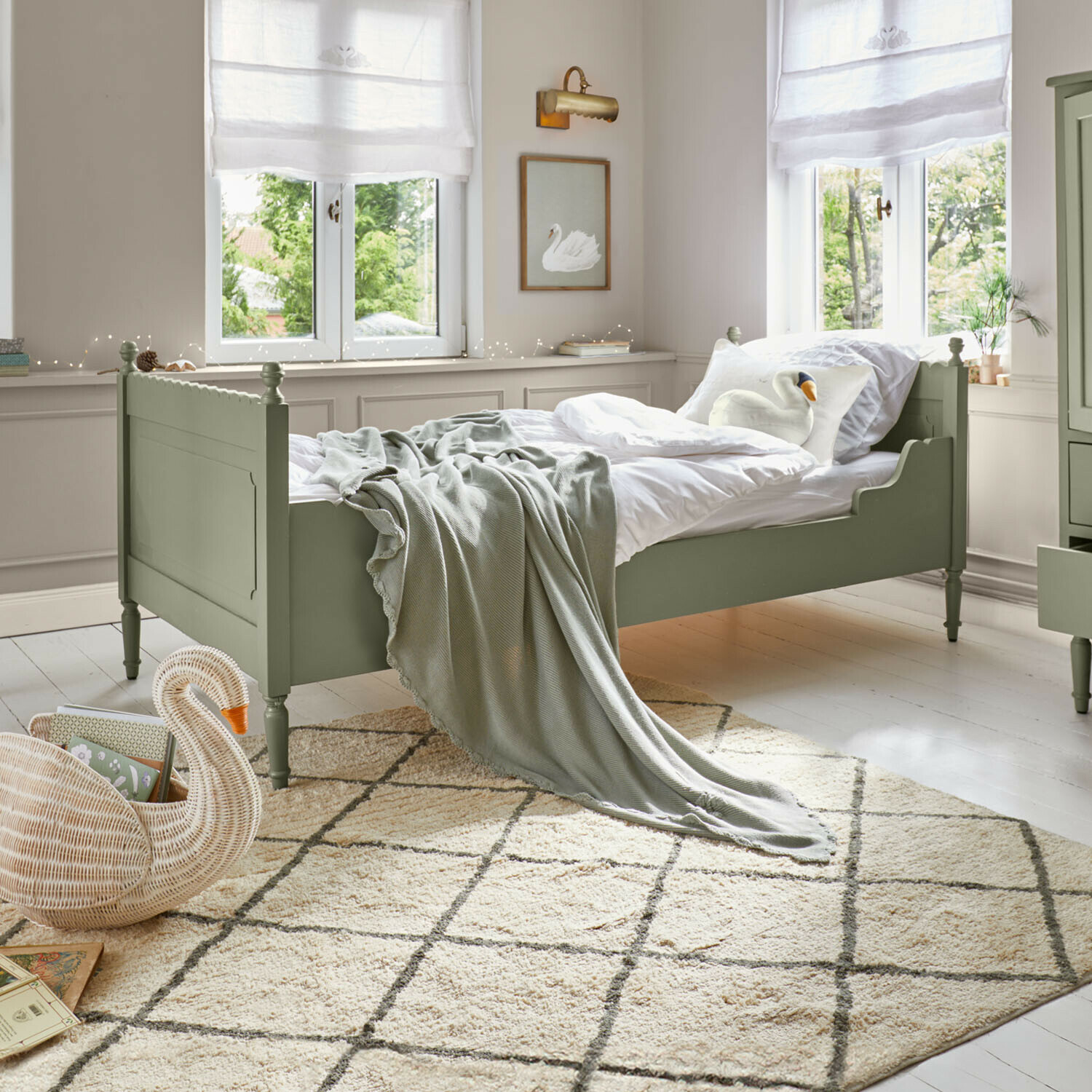 Groen houten bed met wit beddengoed en grijze deken in lichte kamer met patroon vloerkleed