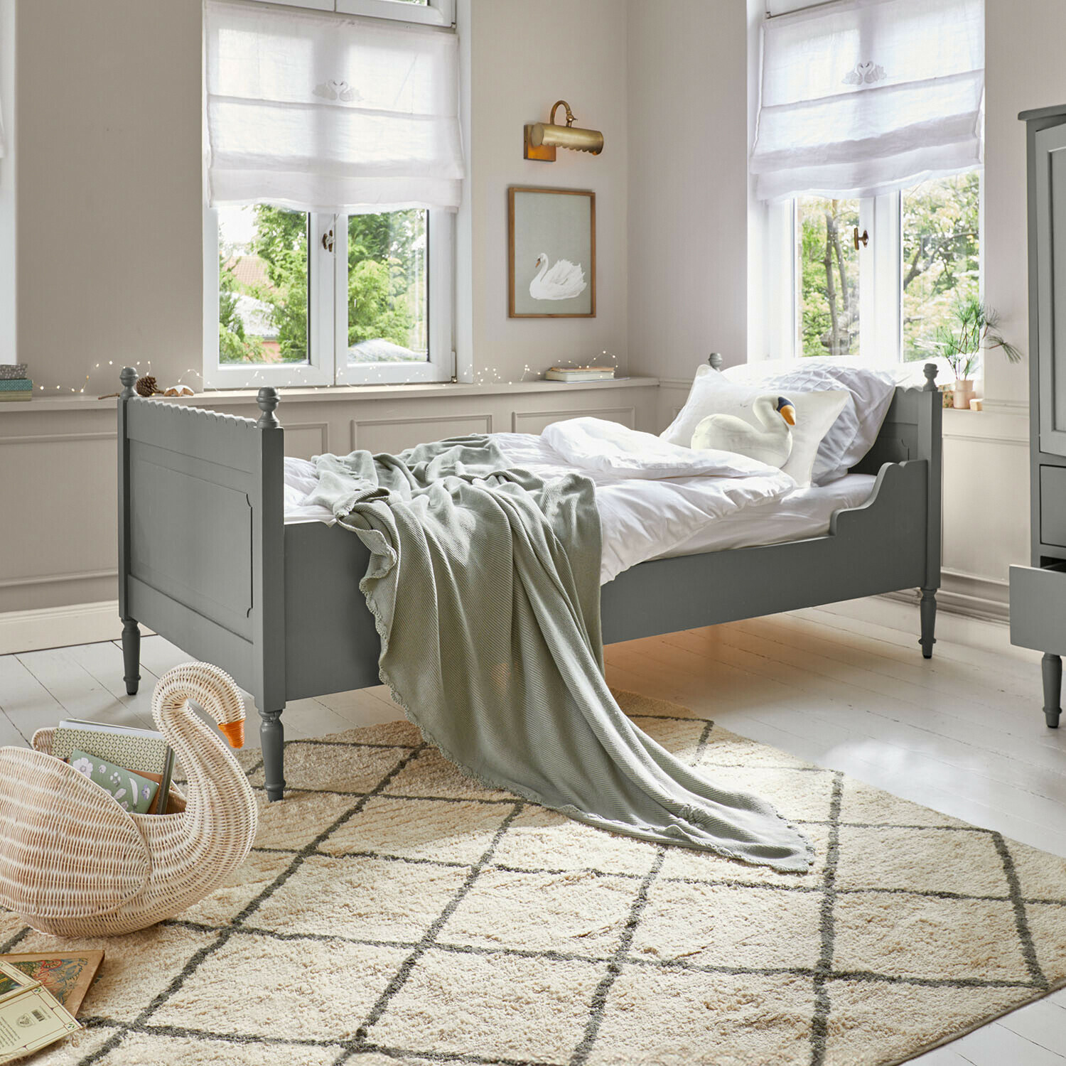 Groen houten bed met wit beddengoed en grijze deken in lichte kamer met patroon vloerkleed
