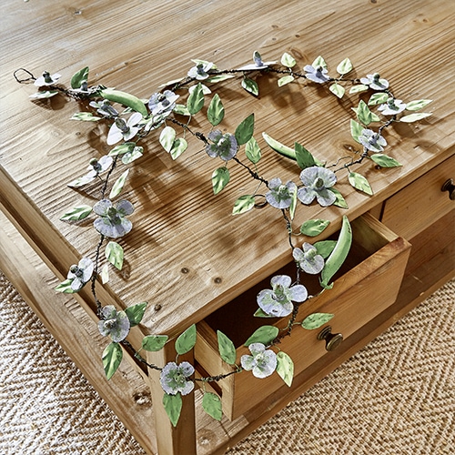 Decoratieve metalen krans met blauwe bloemen en groene bladeren op houten tafel