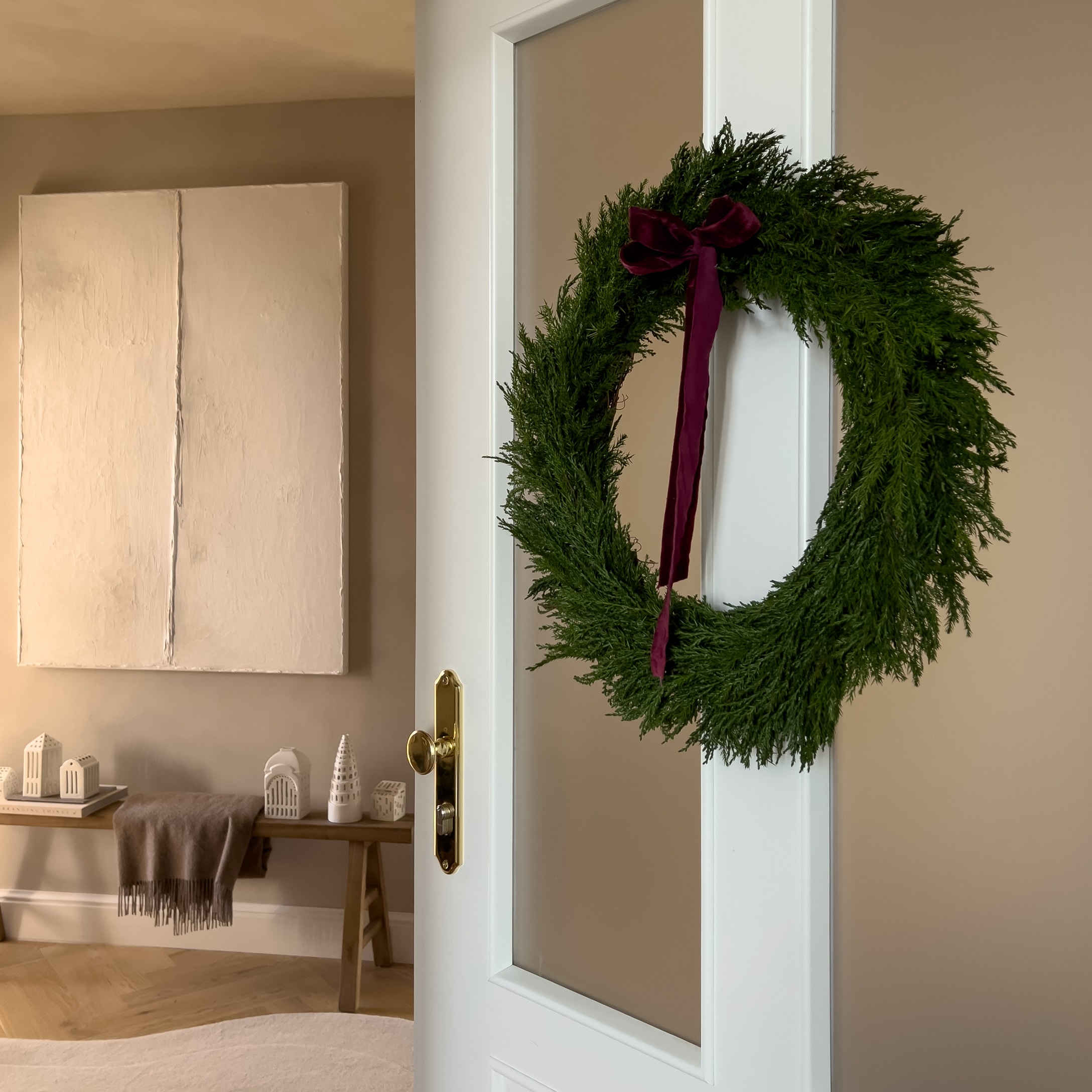 Groene kerstkrans met bordeaux strik aan witte deur in gezellige kamer