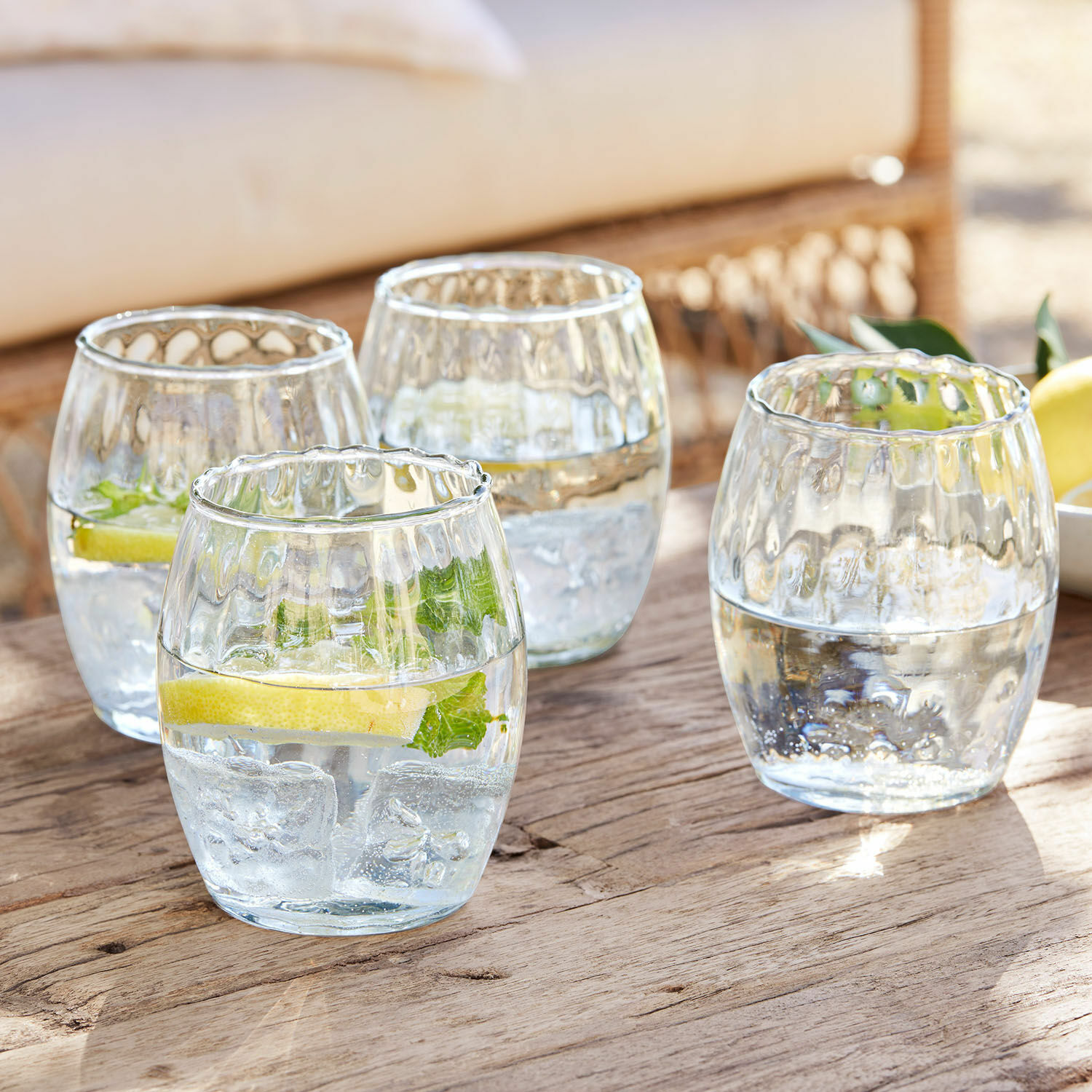 Glas set van 4 Bourgavin Set van vier glazen van helder glas met water, ijs en citroen op een houten tafel