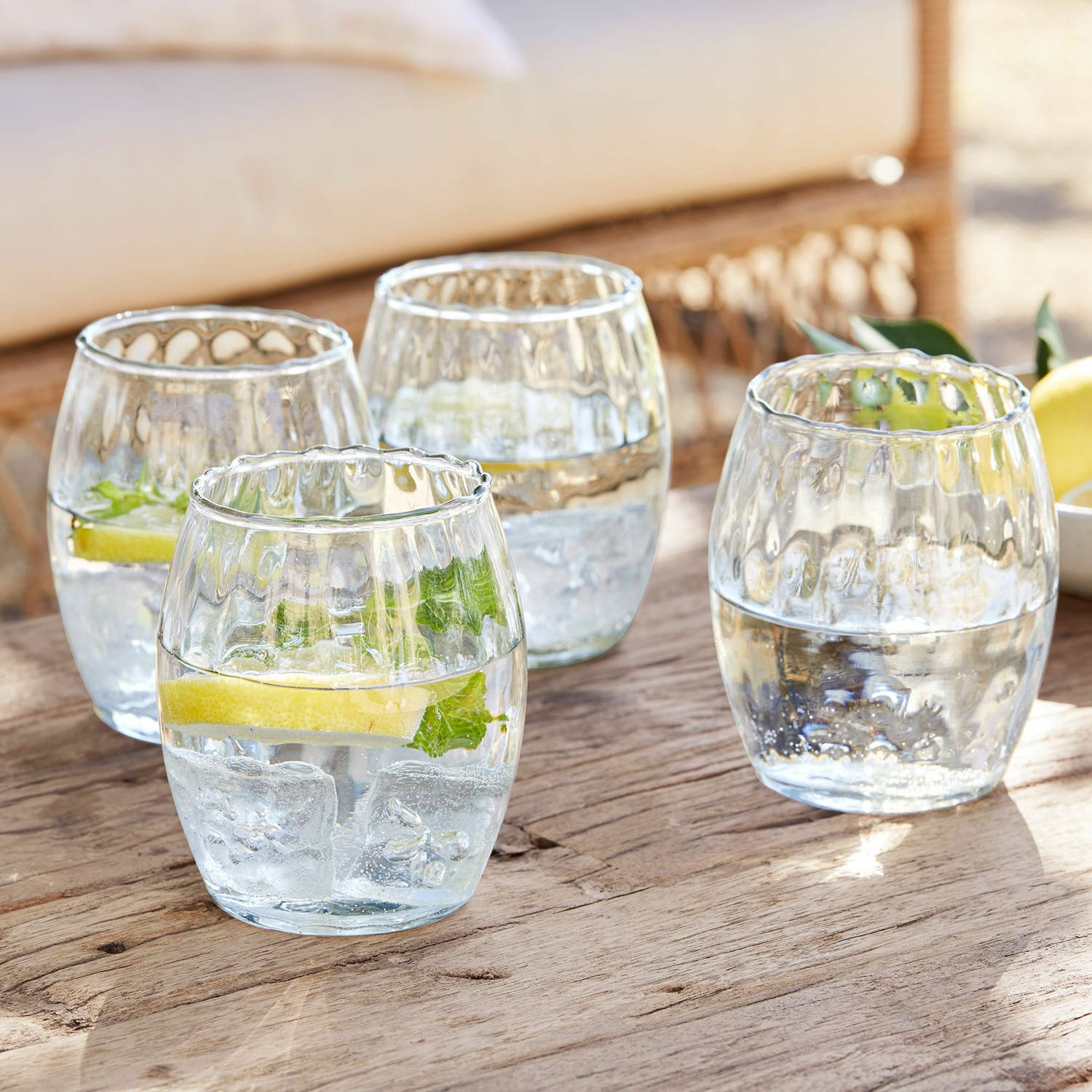 Glas set van 4 Bourgavin Set van vier glazen van helder glas met water, ijs en citroen op een houten tafel