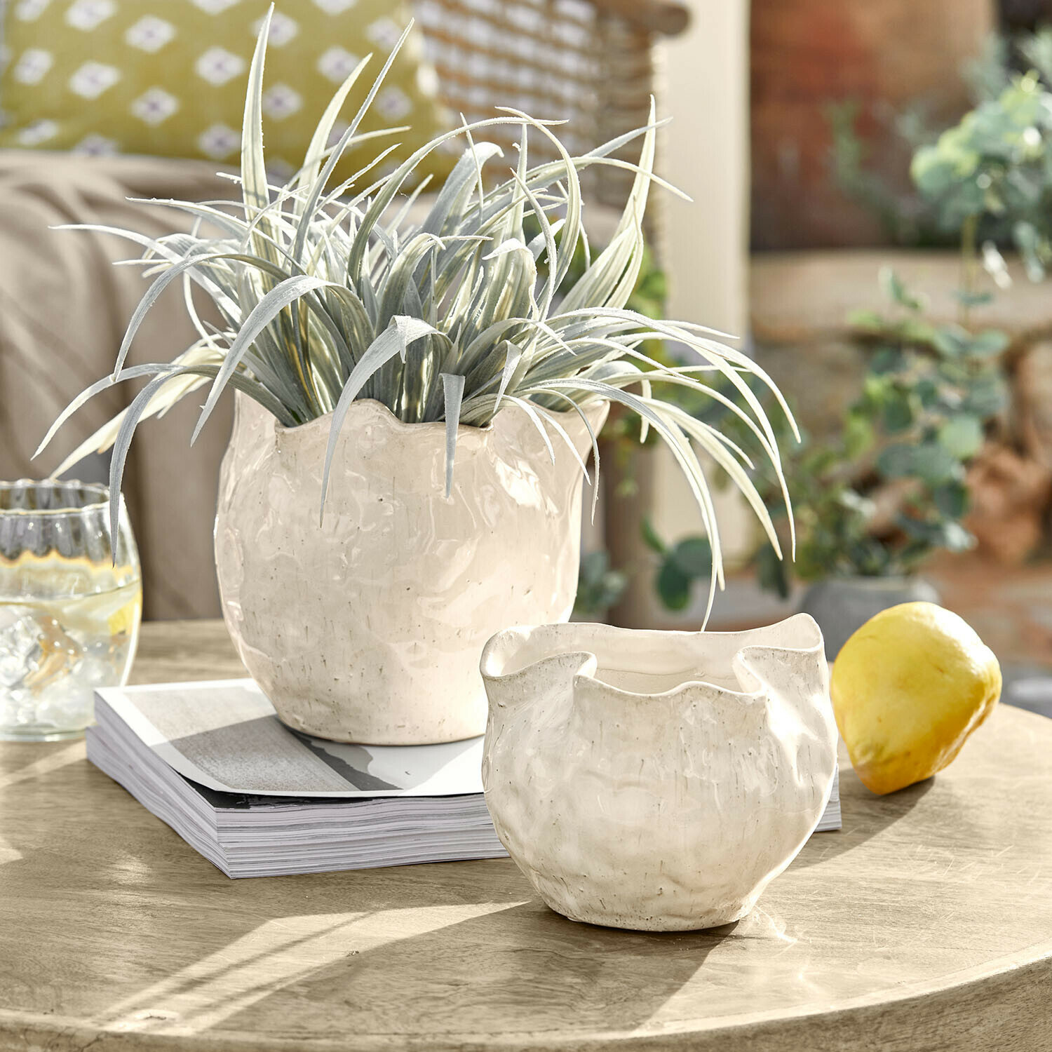 Witte keramische potten met onregelmatige vorm op houten tafel met groene plant en citroen