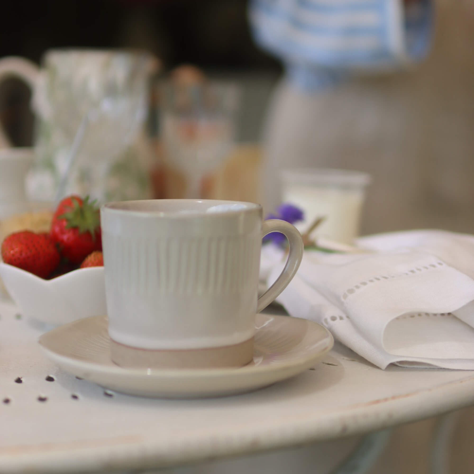 Beige keramische kop en schotel op witte tafel met aardbeien en linnen servet