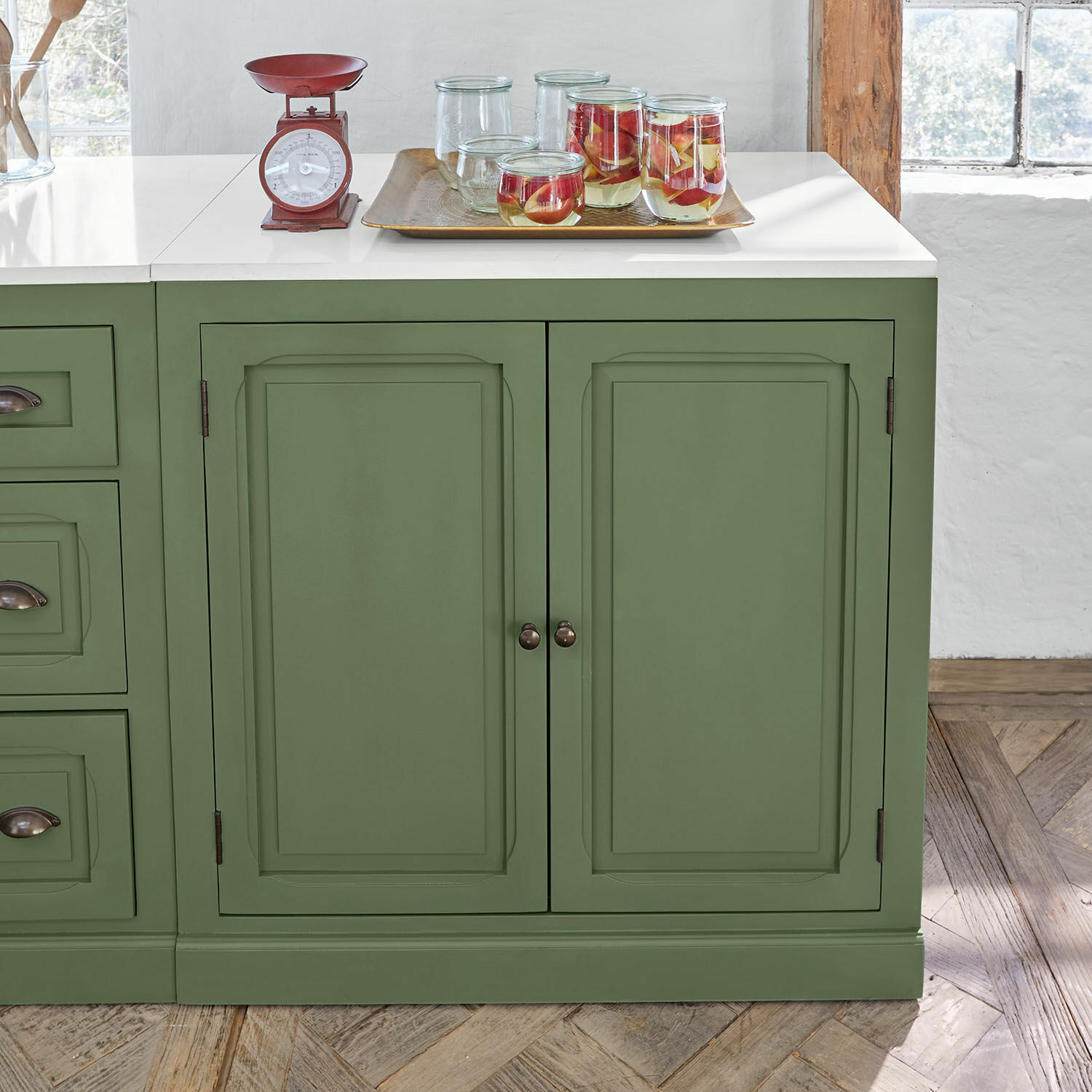 Groene houten keukenkast met wit blad en rode metalen keukenweegschaal erop